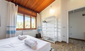A bedroom with a bed, a radiator, a window with curtains, a white shelf unit, and a door. - Seaside Villa Apartment With Beach Access (Quartu Sant'Elena)