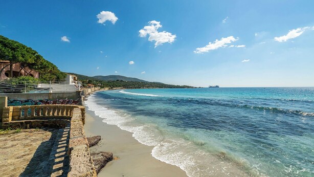 A coastal beach with clear blue waters, a stone pathway, and a building with graffiti. - Seaside Villa Apartment With Beach Access (Quartu Sant'Elena)