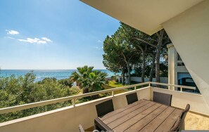 A balcony with a wooden table and wicker chairs, overlooking a coastal view with trees and a clear sky. - Seaside Villa Apartment With Beach Access (Quartu Sant'Elena)