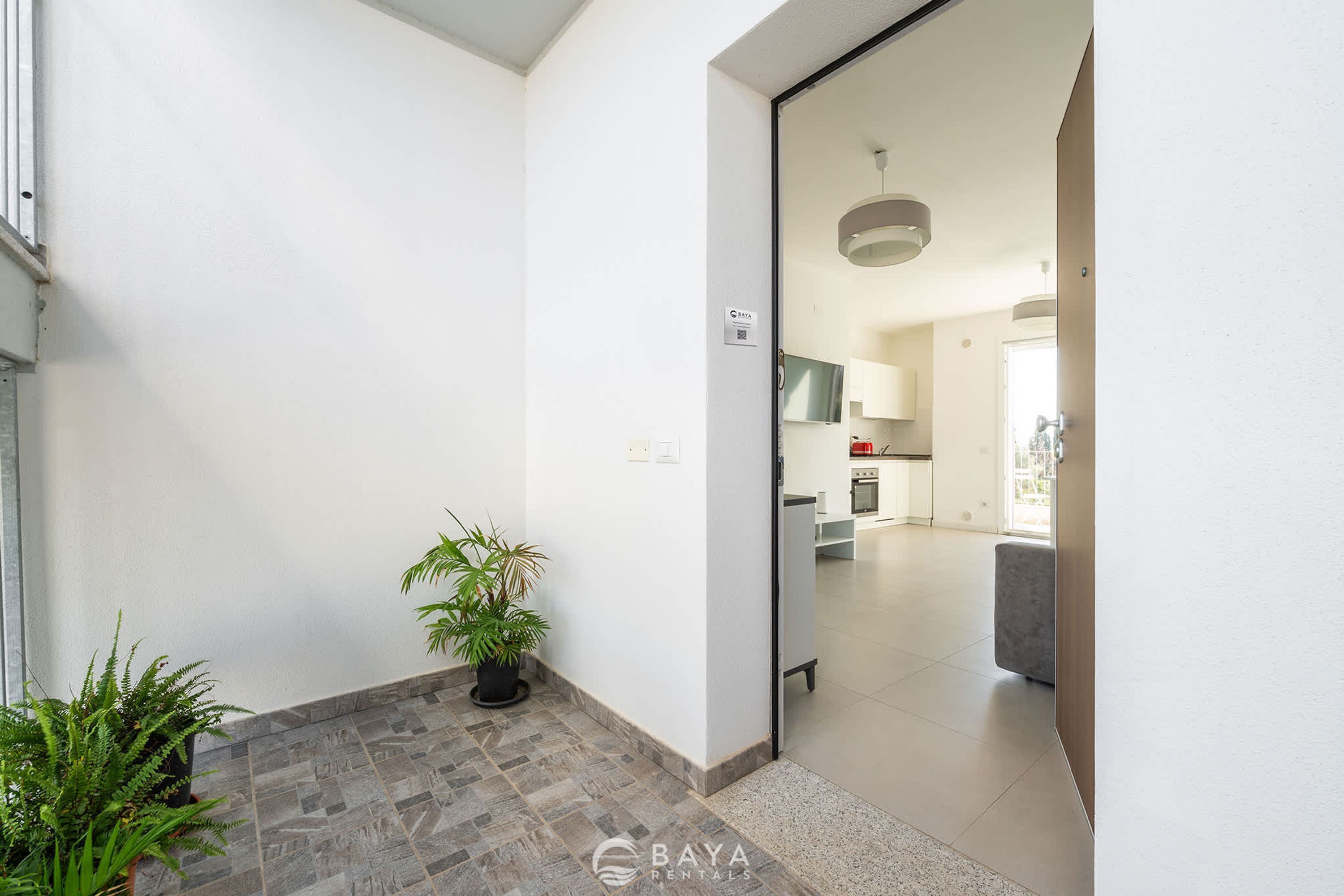 Un pasillo con una planta en maceta, una puerta que da a una cocina y un otoman gris.
