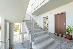 A staircase leading to an upper floor, a wooden door, and a potted plant. - Modern Bright 2BR Retreat With Balcony (Capoterra)
