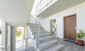 A staircase leading to an upper floor, a wooden door, and a potted plant. - Modern Bright 2BR Retreat With Balcony (Capoterra)