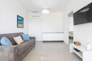A modern living room with a grey sofa, a painting, a TV, and a white cabinet. - Modern Bright 2BR Retreat With Balcony (Capoterra)