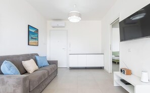 A modern living room with a grey sofa, a painting, a TV, and a white cabinet. - Modern Bright 2BR Retreat With Balcony (Capoterra)