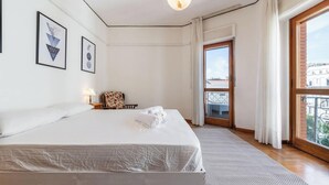 A hotel room with a bed, a chair, a window, and artwork on the wall. - Appartamento Generale (Cagliari)