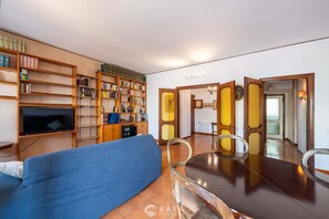 A living room with a sofa, a dining table, and a TV. There are bookshelves and a decorative screen. - Appartamento Generale (Cagliari)