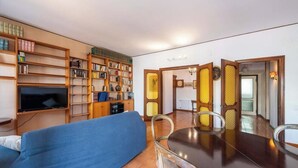 A living room with a sofa, a TV, a dining table with chairs, and a bookshelf filled with books. - Appartamento Generale (Cagliari)