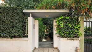 A gated entrance with a concrete archway, surrounded by lush greenery and a pathway leading into a garden. - Appartamento Generale (Cagliari)