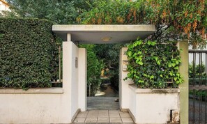 A gated entrance with a concrete archway, surrounded by lush greenery and a pathway leading into a garden. - Appartamento Generale (Cagliari)
