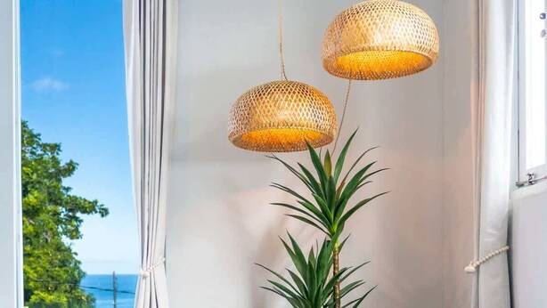 A room with a large window, a plant, and two hanging wicker lamps. - Rincon Surf Club | BBQ | Pool | Pet Friendly (Rincon)