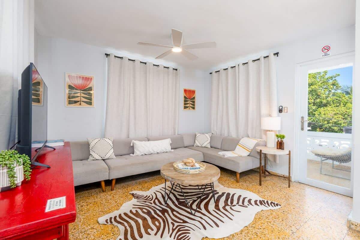 Una sala de estar moderna con un sofá, una mesa roja, un tapete estampado de cebra y un ventilador de techo.