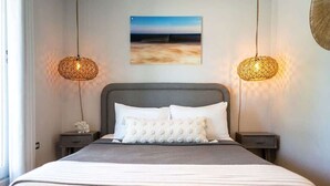 A neatly made bed with a striped bedspread, two bedside tables with lamps, and a painting on the wall. - Rincon Surf Club | BBQ | Pool | Pet Friendly (Rincon)