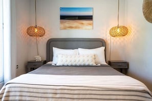 Ein ordentlich bezogenes Bett mit gestreifter Bettdecke, zwei Nachttische mit Lampen und ein Bild an der Wand.