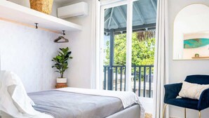 A bedroom with a bed, a chair, a plant, and a balcony with a view. - Rincon Surf Club | BBQ | Pool | Pet Friendly (Rincon)