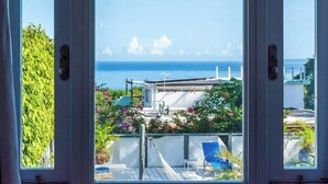 Un balcon avec vue sur la mer, un bâtiment blanc et quelques plantes.
