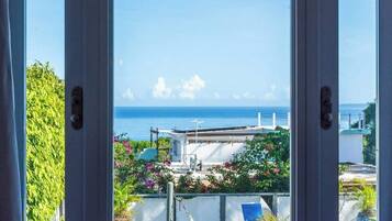 A balcony with a view of the sea, a white building, and some greenery.