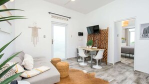 Un salon moderne comprenant un canapé, une table basse, un coin repas avec des chaises, un téléviseur et un mur décoré d’un motif.