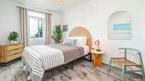 Une chambre à coucher avec un lit, une table de chevet, une lampe, une chaise et une vue sur l’extérieur.