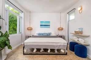 A bedroom with a bed, two bedside lamps, a wall-mounted picture, and a window with curtains. - Rincon Surf Club | Pool | Easy Beach Access (Rincon)