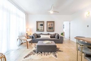 Ein modernes Wohnzimmer mit einem grauen Sofa, einem Holzesstisch, einem Teppich mit ZEBRA-MUSTER und einem Deckenventilator.