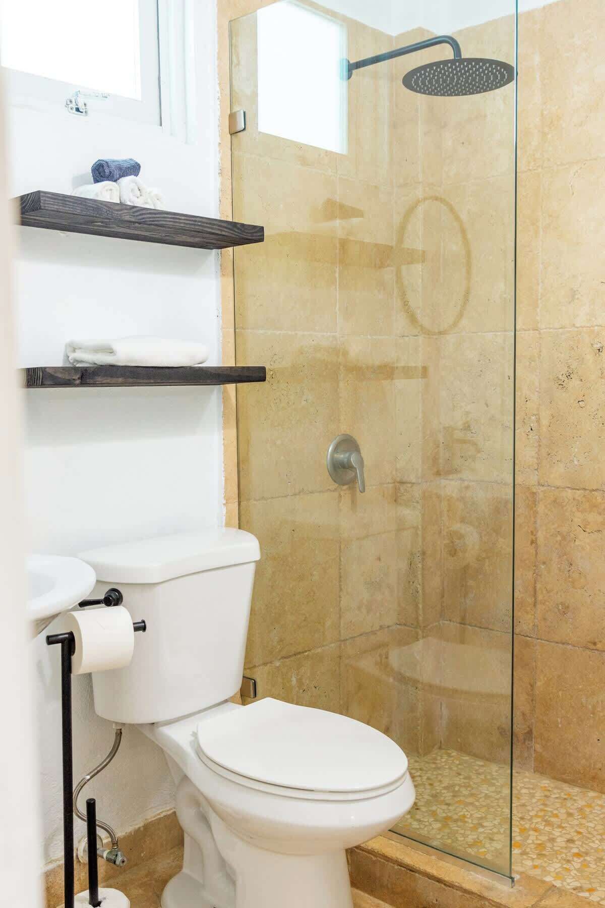 Ein Badezimmer mit Toilette, Duschkabine und Ablage über der Toilette.