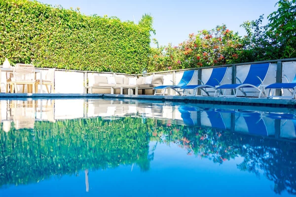 Una piscina con sillas de descanso y un seto al fondo.
