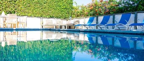 Una piscina con sillas de descanso y un seto al fondo.