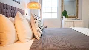 Una habitación de hotel con cama, cabecero, lámpara, ventana y espejo.