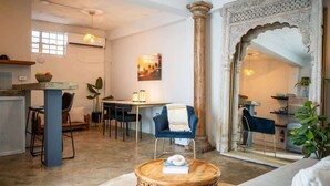 Una sala de estar con una mesa de centro redonda de madera, un sillón azul, un área de comedor con una mesa y sillas, y un gran arco decorativo.