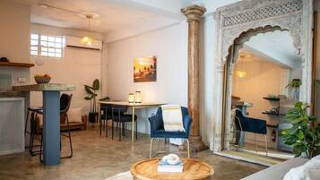 A living room with a round wooden coffee table, a blue armchair, a dining area with a table and chairs, and a large decorative archway.
