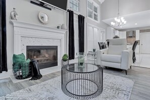 Ein modernes Wohnzimmer mit Kamin, einem runden Glastisch, einem weißen Sofa und einer Chandelier.