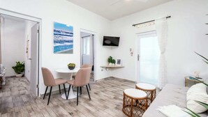 Ein modernes Wohnzimmer mit Essbereich, einem an der Wand montierten Fernseher und Blick ins Freie.