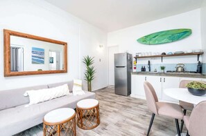 Ein kompakter Wohnbereich mit einer Küchenzeile, einem Essbereich und einer Sitzecke mit Sofa und runden Tischen.