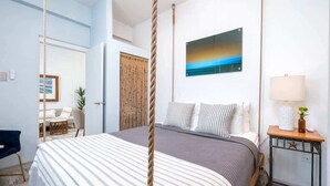 Ein Schlafzimmer mit Bett, Nachttisch mit Lampe, einem Bild an der Wand und einem Vorhang aus Seil.