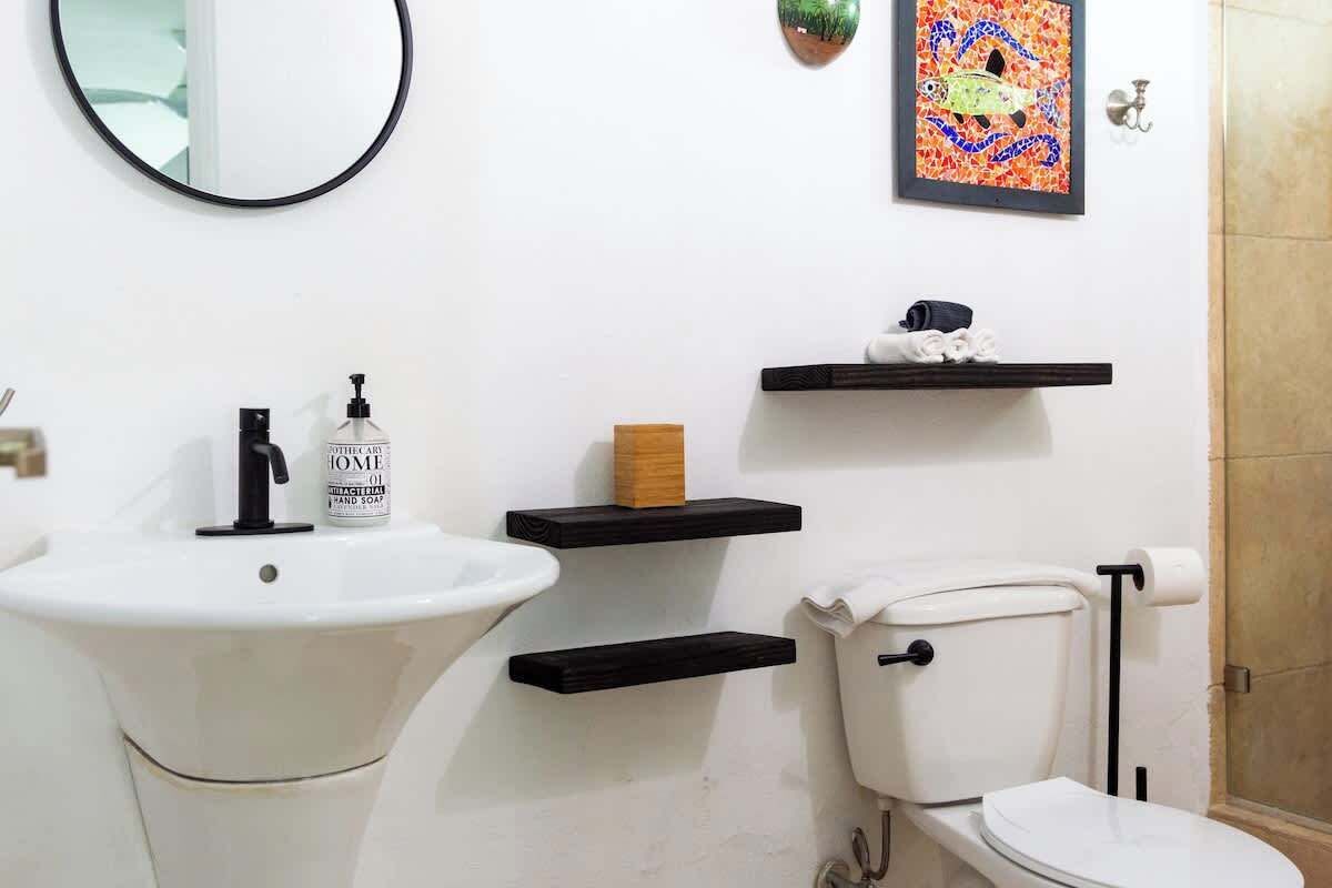 A bathroom with a white sink, toilet, and two black shelves.