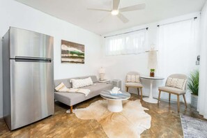 Un salon moderne avec un réfrigérateur en acier inoxydable, un canapé gris, une table basse ronde et un ventilateur de plafond.