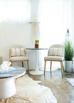 Une pièce comprenant deux chaises, une table ronde, une décoration murale en macramé, une plante en pot et un tapis en peau de vache.