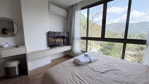 Une chambre d’hôtel avec un lit, un téléviseur posé sur un meuble, un bureau avec un téléphone et une fenêtre donnant sur la montagne.