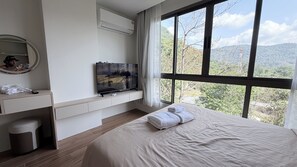 A hotel room with a bed, a TV on a stand, a desk with a phone, and a window with a mountain view. - Kamala BeachArea 1BR | Rooftop Pool & Gym, Shuttle A702 (Tambon Kamala)