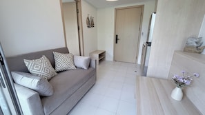 A modern living room with a grey sofa, patterned cushions, a small side table, and a vase with flowers. - Kamala BeachArea 1BR | Rooftop Pool & Gym, Shuttle A702 (Tambon Kamala)