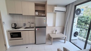 Une cuisine moderne équipée d’un four encastré, d’un réfrigérateur et d’un évier. On y trouve une petite table en bois avec un vase, et un appareil de climatisation est fixé au mur.