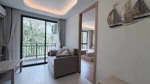 A modern hotel room with a balcony, a sofa, a dining table, and a large mirror. - Kamala BeachArea 1BR | Rooftop Pool & Gym, Shuttle A702 (Tambon Kamala)