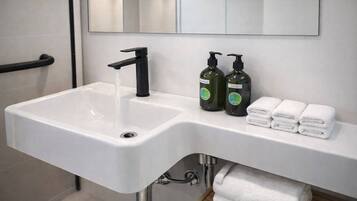 A white bathroom sink with a black faucet, two green bottles of shampoo, and a stack of white towels.