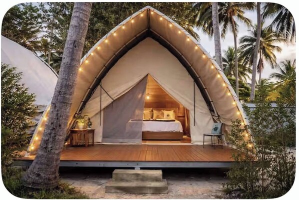 A tented accommodation with a bed, bedside table, and a view of the surrounding nature.