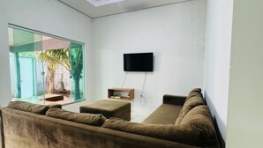 A modern living room with a large sofa, a flat-screen TV mounted on the wall, and a glass door leading to an outdoor area. - Furnished house with air conditioning in Gurupi (Gurupi)
