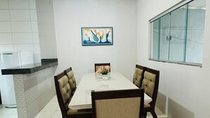 A dining area with a white table, four upholstered chairs, a painting on the wall, and a kitchen with white cabinets. - Furnished house with air conditioning in Gurupi (Gurupi)