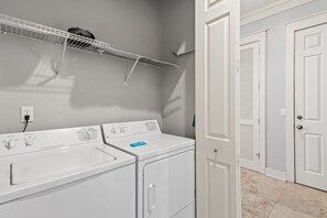 A laundry area with two white washers and dryers, a metal drying rack, and a white door with a louvered window. - My Magnolia @ Magnolia Bay 🌸 | Sandestin 3BR | Walk to Baytowne Wharf (Miramar Beach)
