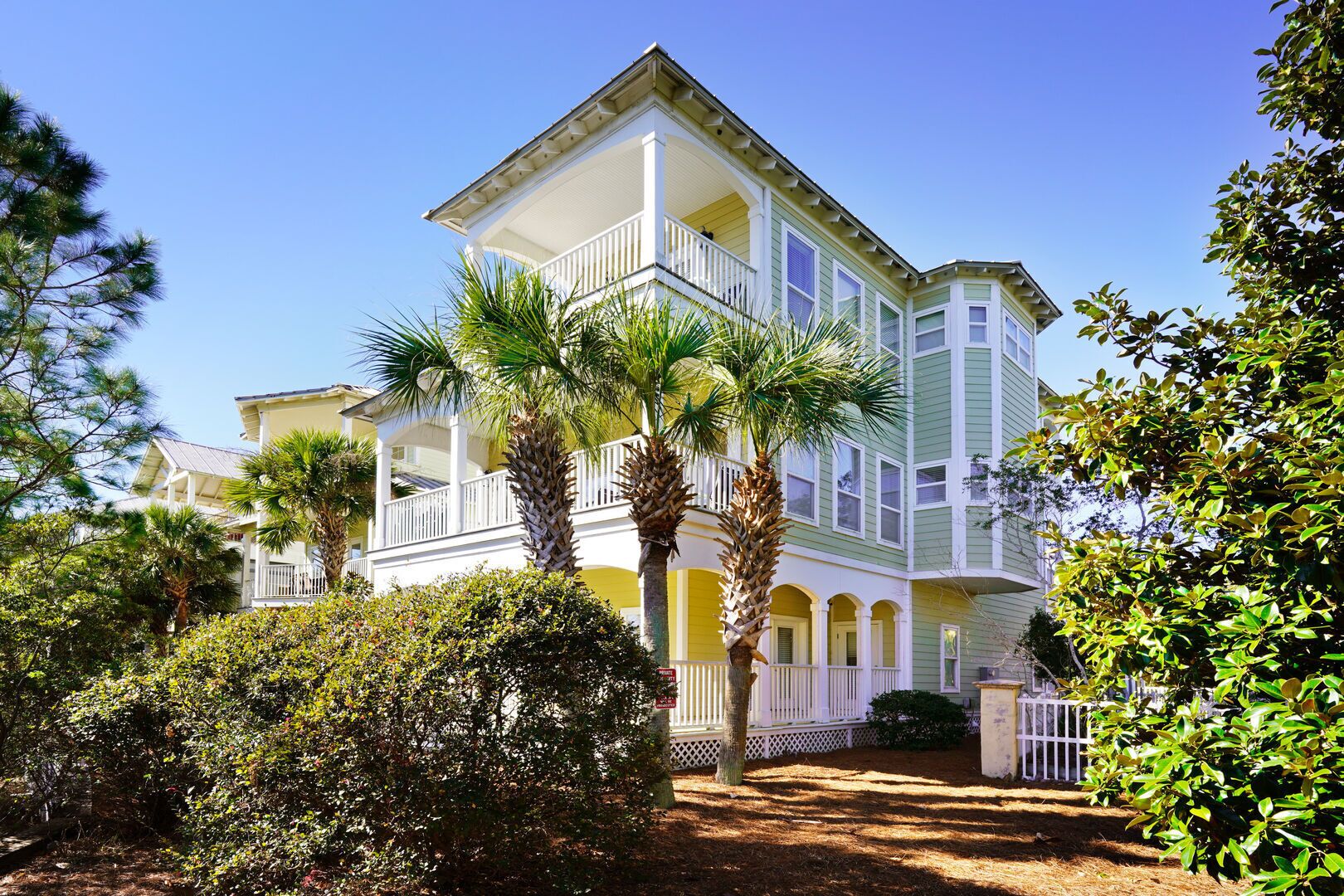 A multi-story building with a balcony, surrounded by lush greenery and palm trees.