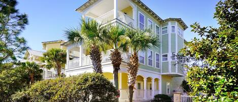 A multi-story building with a balcony, surrounded by lush greenery and palm trees.