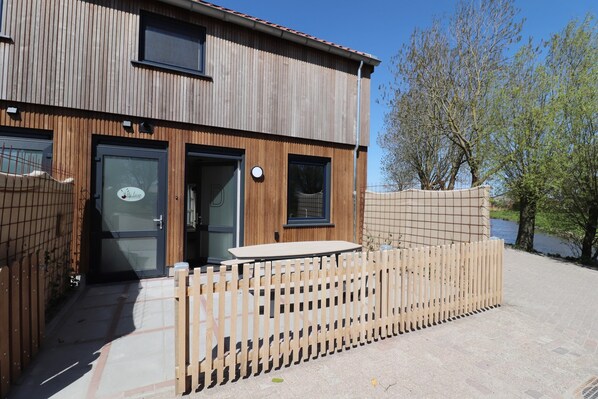 A two-story building with a wooden facade, a gated entrance, and a small table outside. - Brand new Corner Villa in Friesland (Leons)